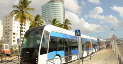 Plusieurs bus en ville avec des personnes qui attendent à un arrêt.