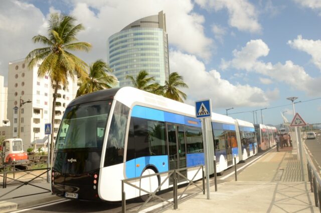 Plusieurs bus en ville avec des personnes qui attendent à un arrêt.